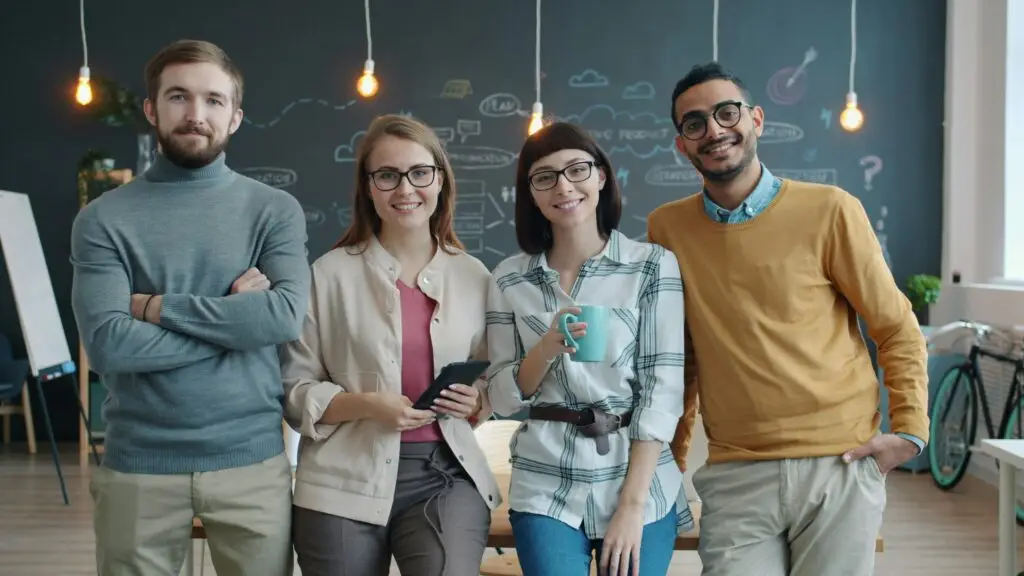 Four diverse professionals smiling and collaborating in a modern office with an illustrated chalkboard background, representing Penda Aiken Inc.’s commitment to MWBE-certified staffing and inclusive workplace culture.